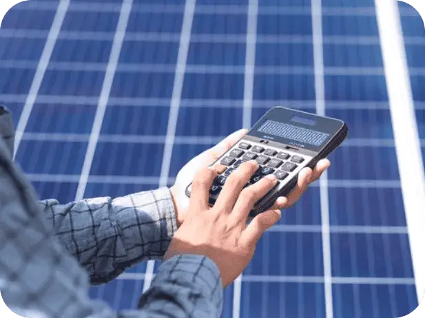Person using a calculator near solar panels for energy monitoring.