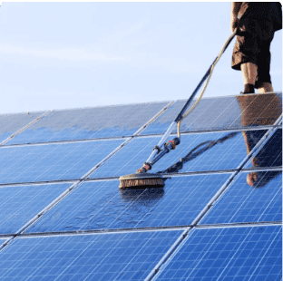 Technician cleaning solar panels on a rooftop with a brush and hose.